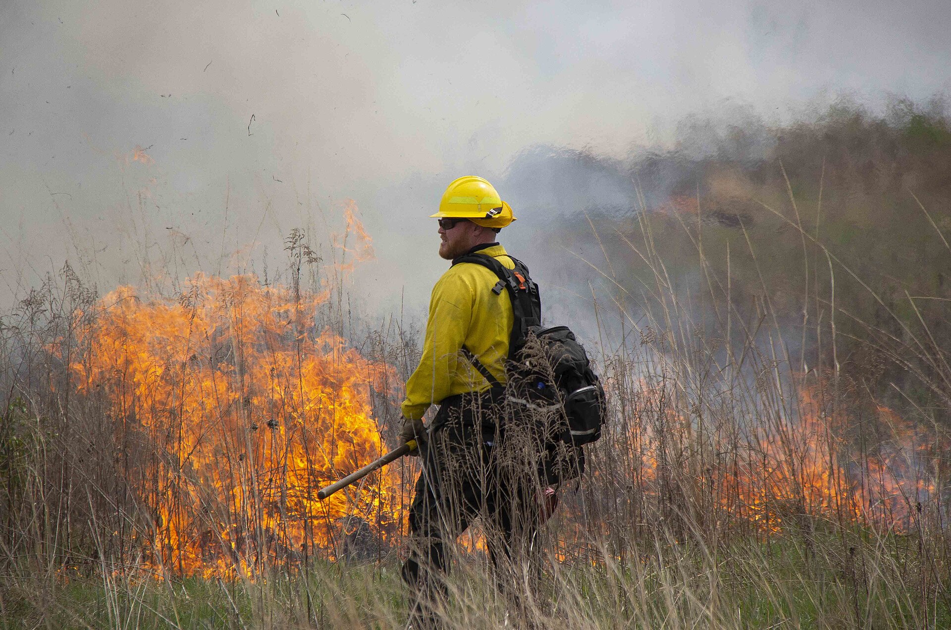 A firefighter opening a control line with a drip torch across a field.